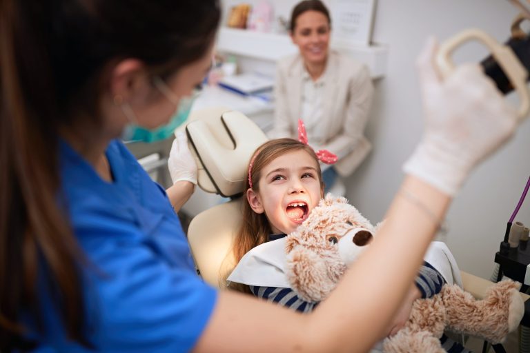 Young girl smiling during a dental exam while holding a stuffed animal.